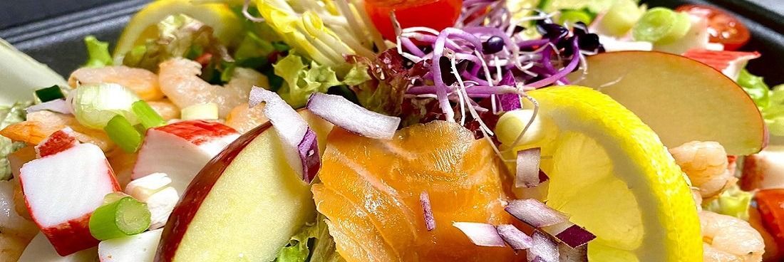 Een kleurrijke zeevruchtensalade met garnalen, krabsticks, gerookte zalm, appelschijfjes, rode ui en citroenpartjes.