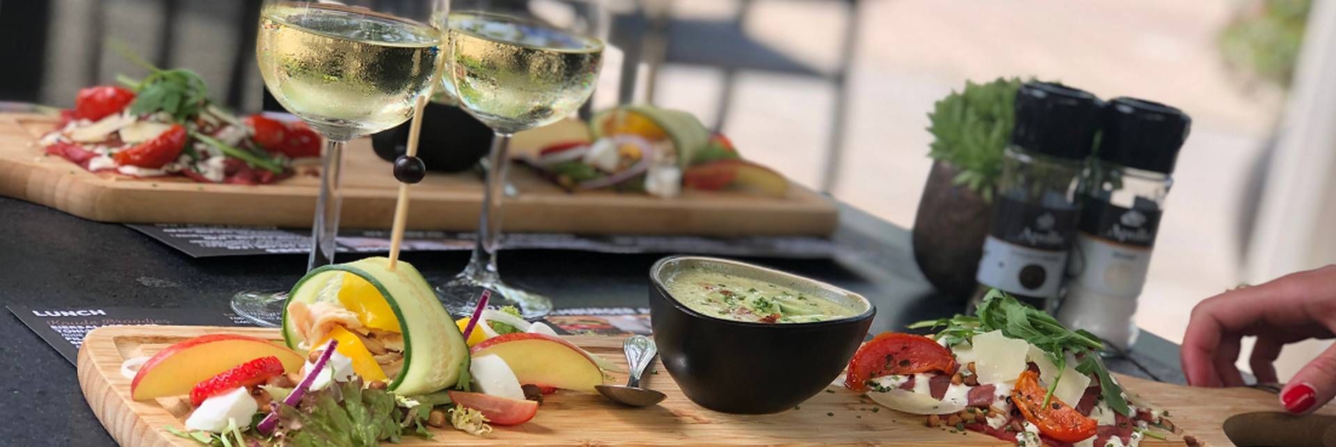 Houten planken, belegd met vers fruit, kaas en een dipsausje, staan uitgestald op een tafel met glazen witte wijn.
