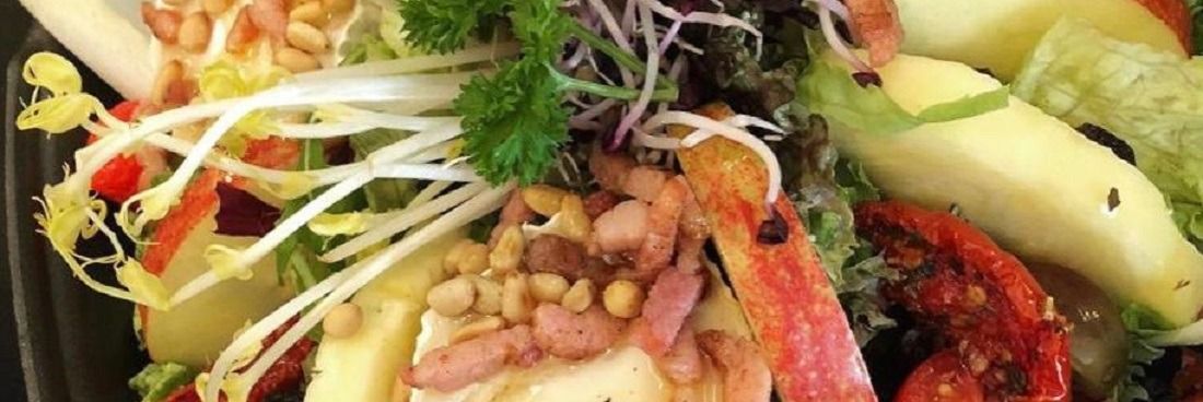 Een frisse salade met geitenkaas, spek en pijnboompitten, gemengde sla, taugé en sch schijfjes appel.