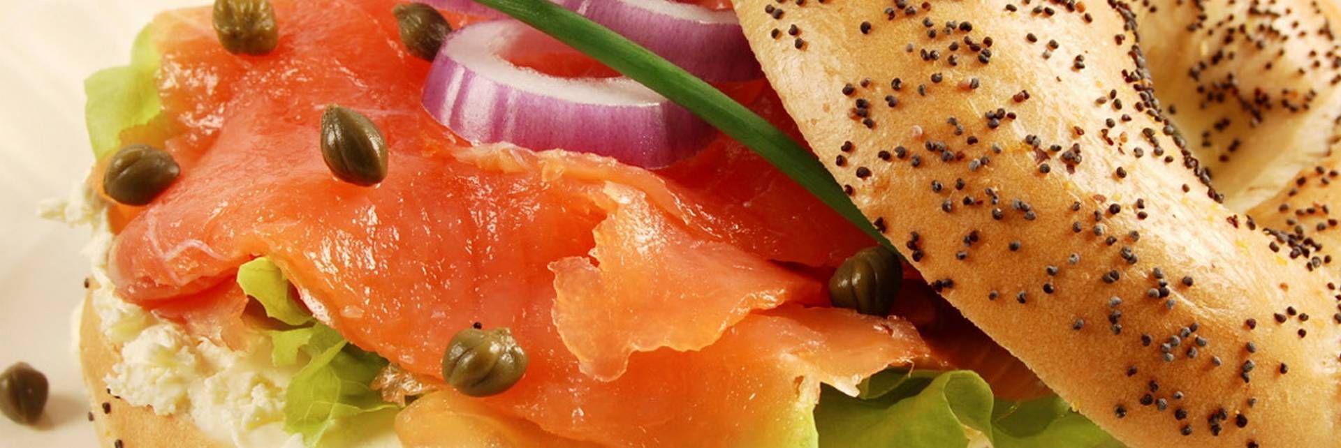 Een bagel met maanzaad, belegd met gerookte zalm, roomkaas, rode ui, kappertjes en verse bieslook.