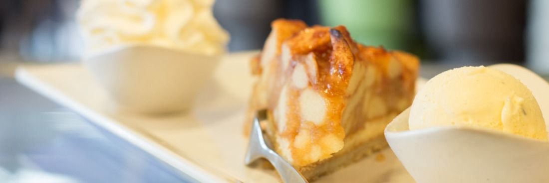 Een stuk appeltaart geserveerd met een bolletje vanille-ijs en een toefje slagroom op een bord.