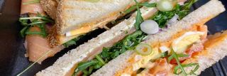 Twee geroosterde sandwiches met zalm en ei op volkorenbrood met rucola, geserveerd op een donker bord.