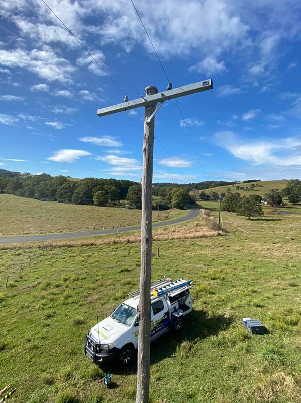 A White Truck is Parked Next to a Wooden Pole in a Grassy Field — Mick Sawtell Electrical Pty Ltd in South Lismore, NSW