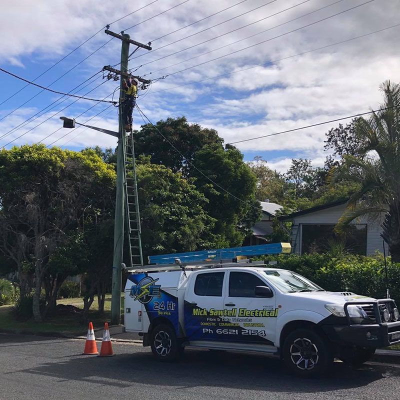 A Man on a Ladder is Working on a Power Pole Next to a Truck — Mick Sawtell Electrical Pty Ltd in South Lismore, NSW