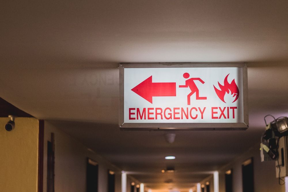 An Emergency Exit Sign is Hanging From the Ceiling of a Hallway — Mick Sawtell Electrical Pty Ltd in South Lismore, NSW