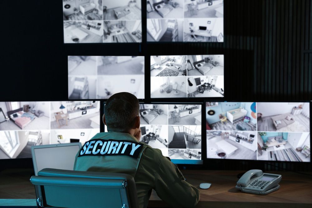 A Security Guard is Sitting at a Desk in Front of a Wall of Monitors — Mick Sawtell Electrical Pty Ltd in Burleigh Heads, QLD