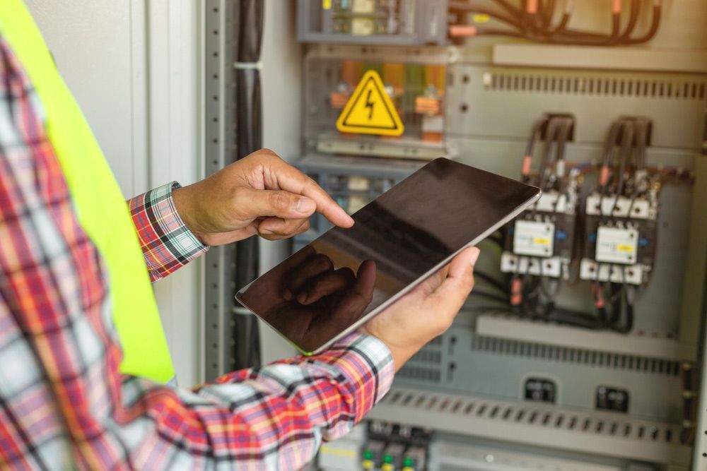 A Man is Holding a Tablet in His Hands in Front of an Electrical Box — Mick Sawtell Electrical Pty Ltd in South Lismore, NSW