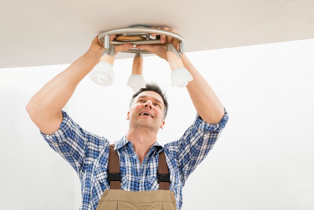 A Man is Installing a Light Fixture on the Ceiling — Mick Sawtell Electrical Pty Ltd in Kingscliff, NSW