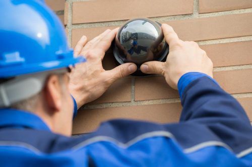 A Man is Installing a Security Camera on a Brick Wall — Mick Sawtell Electrical Pty Ltd in South Lismore, NSW