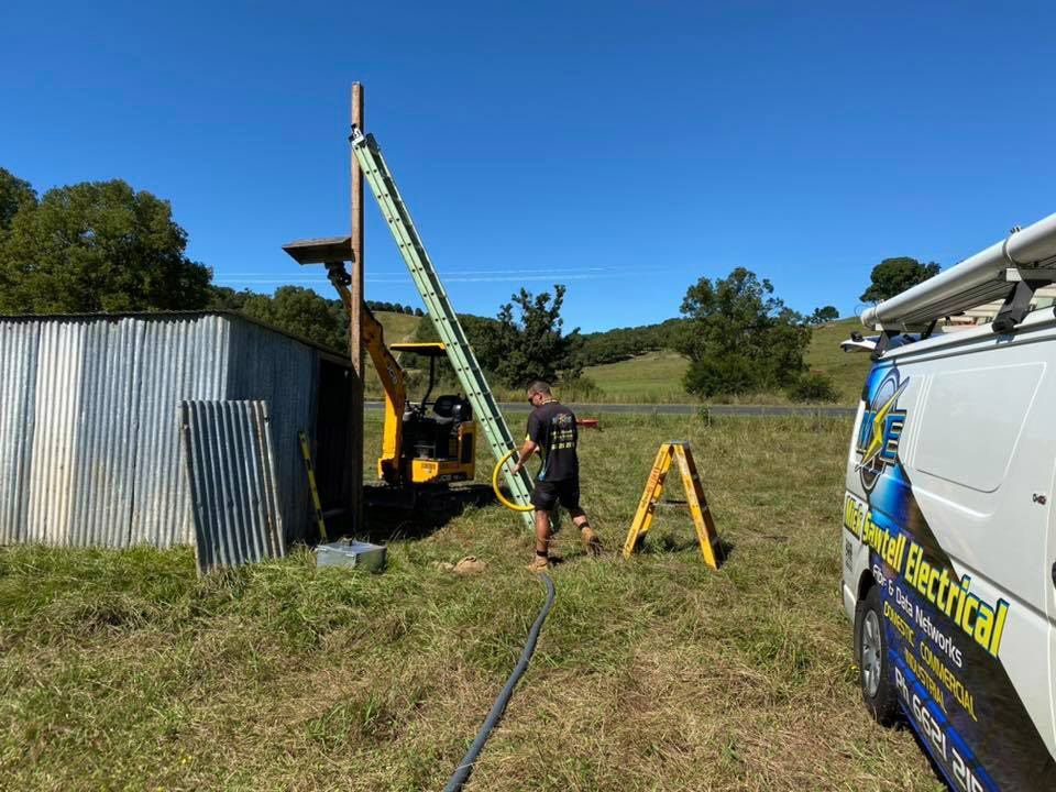 A Man is Standing Next to a Ladder in a Field Next to a Van — Mick Sawtell Electrical Pty Ltd in South Lismore, NSW