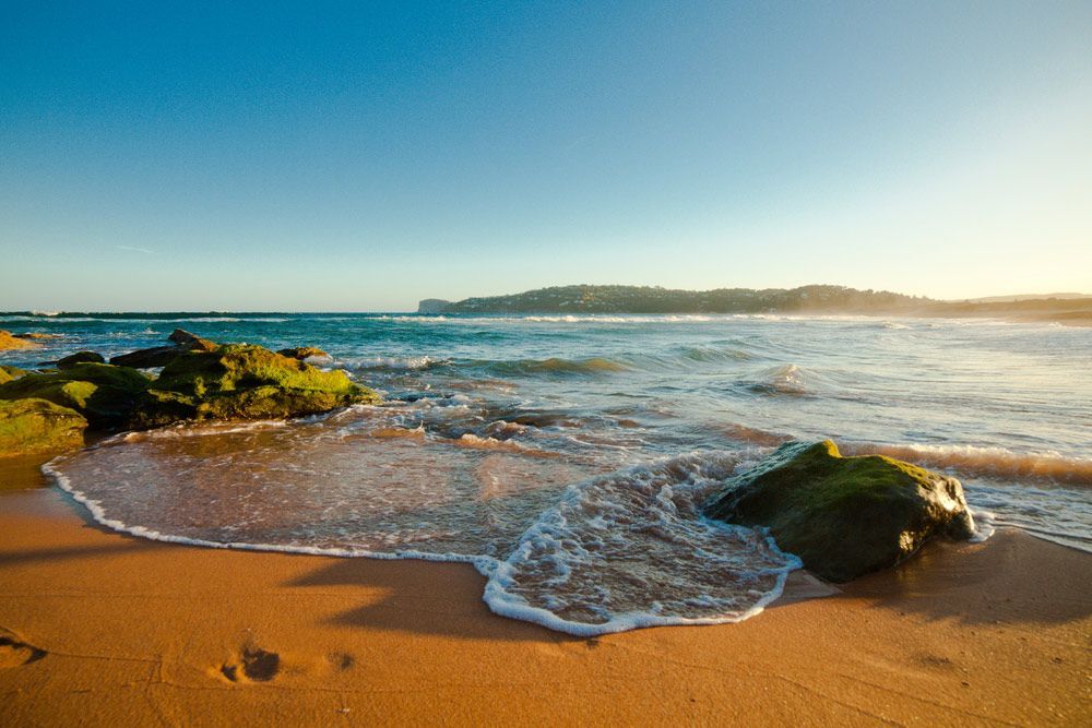A Beach With Rocks and Waves Coming in on a Sunny Day — Mick Sawtell Electrical Pty Ltd in Palm Beach, QLD