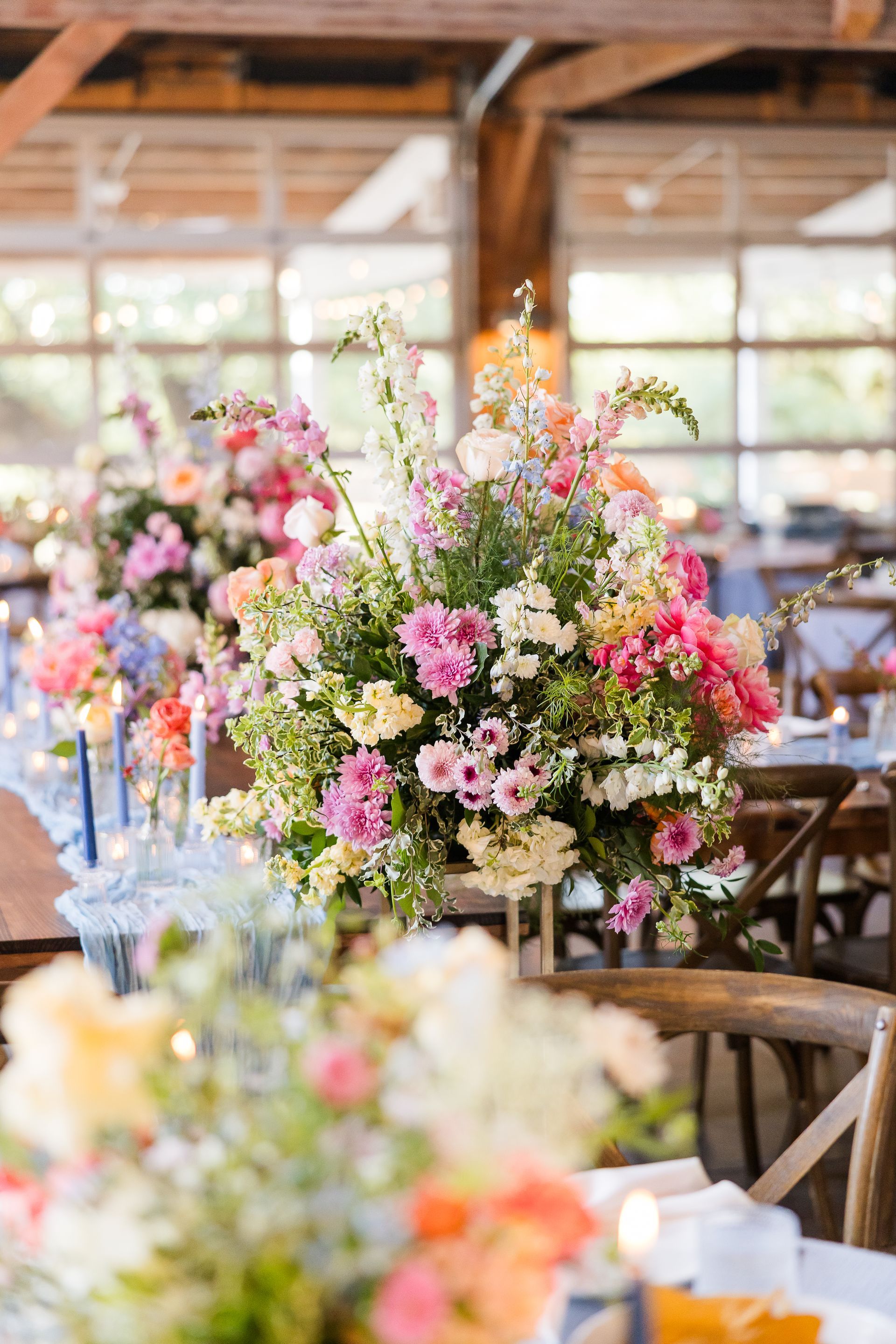 Colorful floral centerpieces on tables in a bright rustic banquet hall
