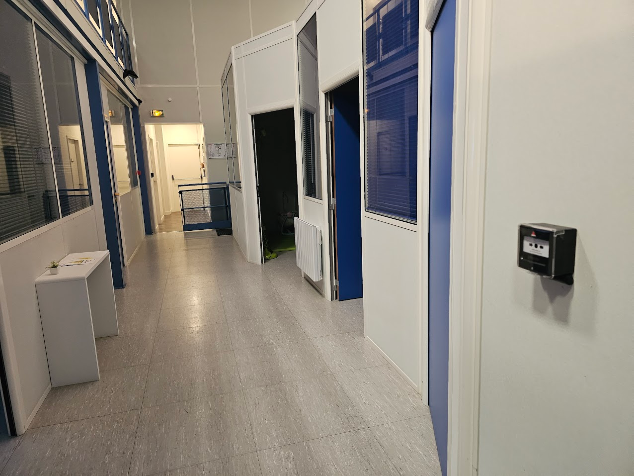 Un long couloir avec des portes bleues et des murs blancs
