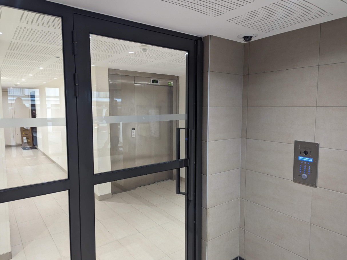 Une porte vitrée dans un immeuble avec un ascenseur en arrière-plan.