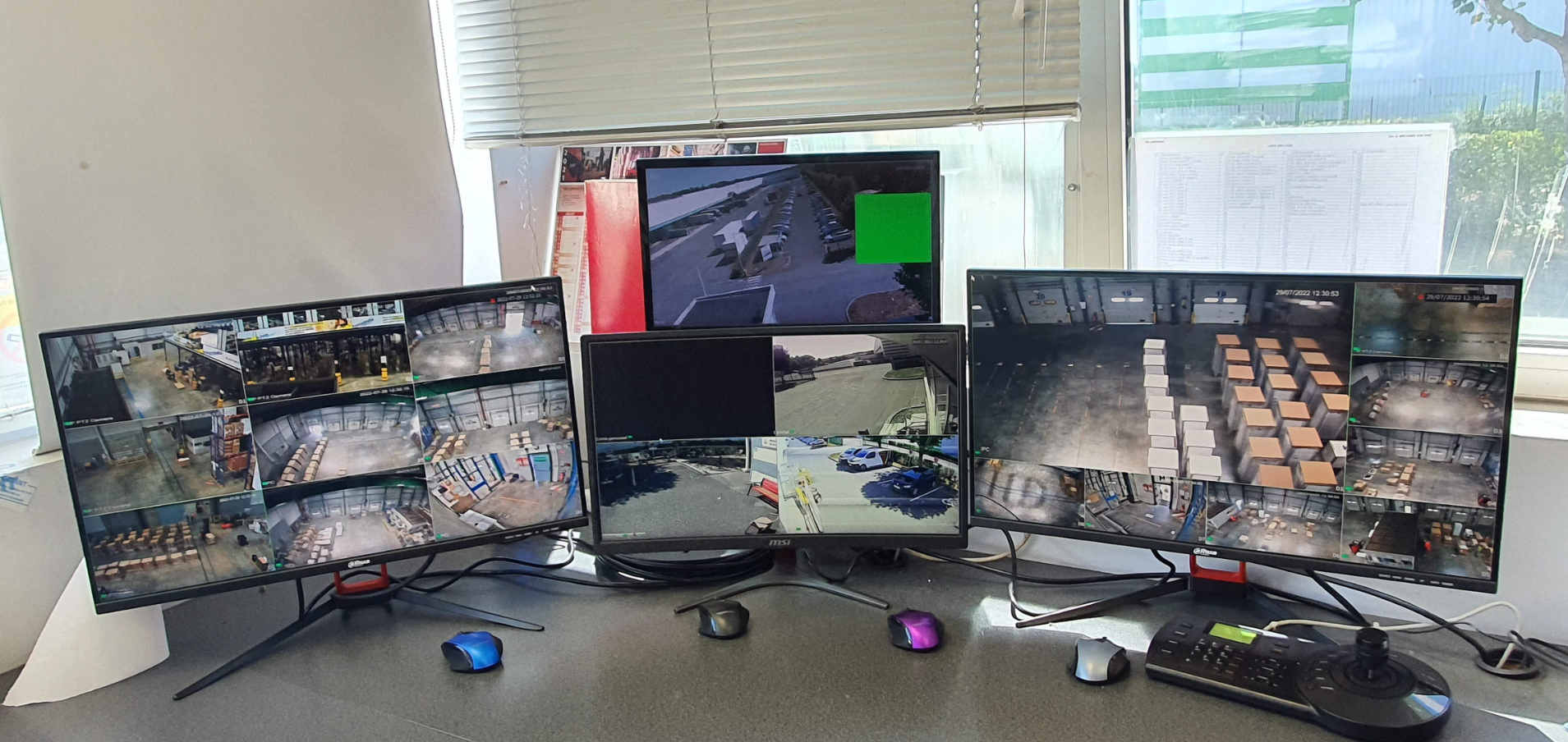 Trois écrans d'ordinateur sont posés sur un bureau devant une fenêtre.