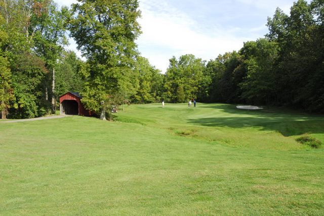 A golf course with a red covered bridge in the background.