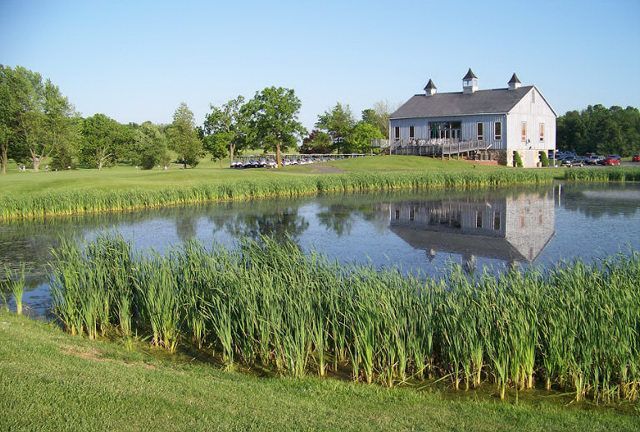 A white barn is reflected in the water of a pond