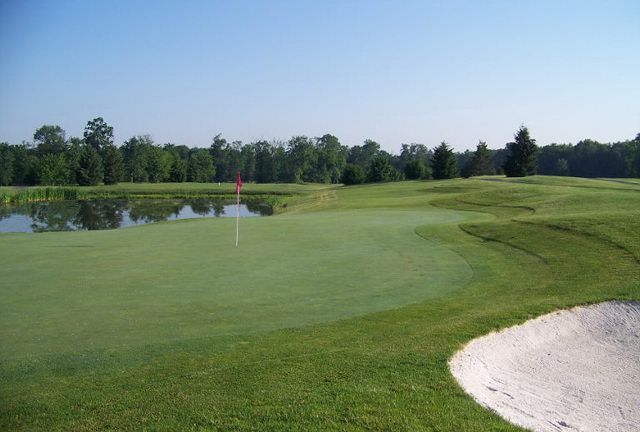 A golf course with a green and a pond in the background.