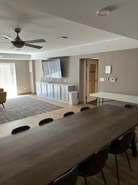 A room with a long table and chairs and a ceiling fan