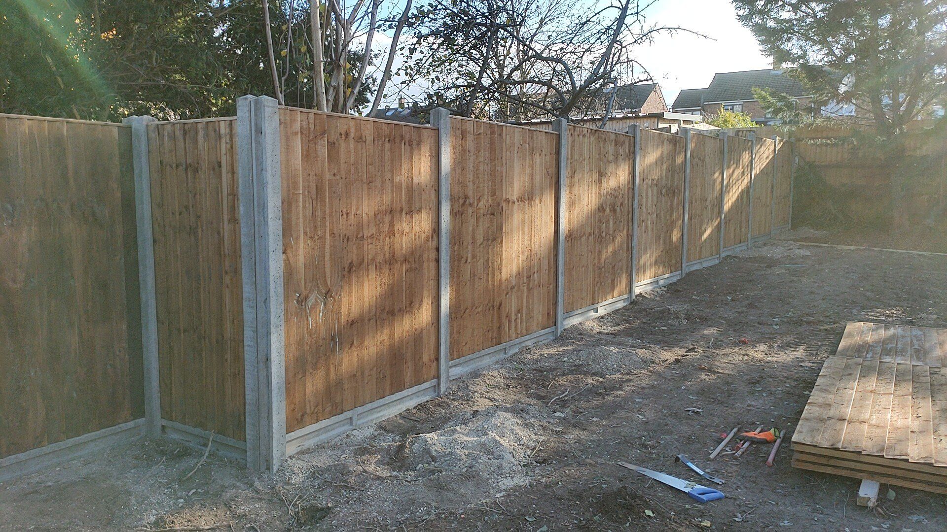 A concrete post and gravel board fence with wooden fence panels as seen from outside.