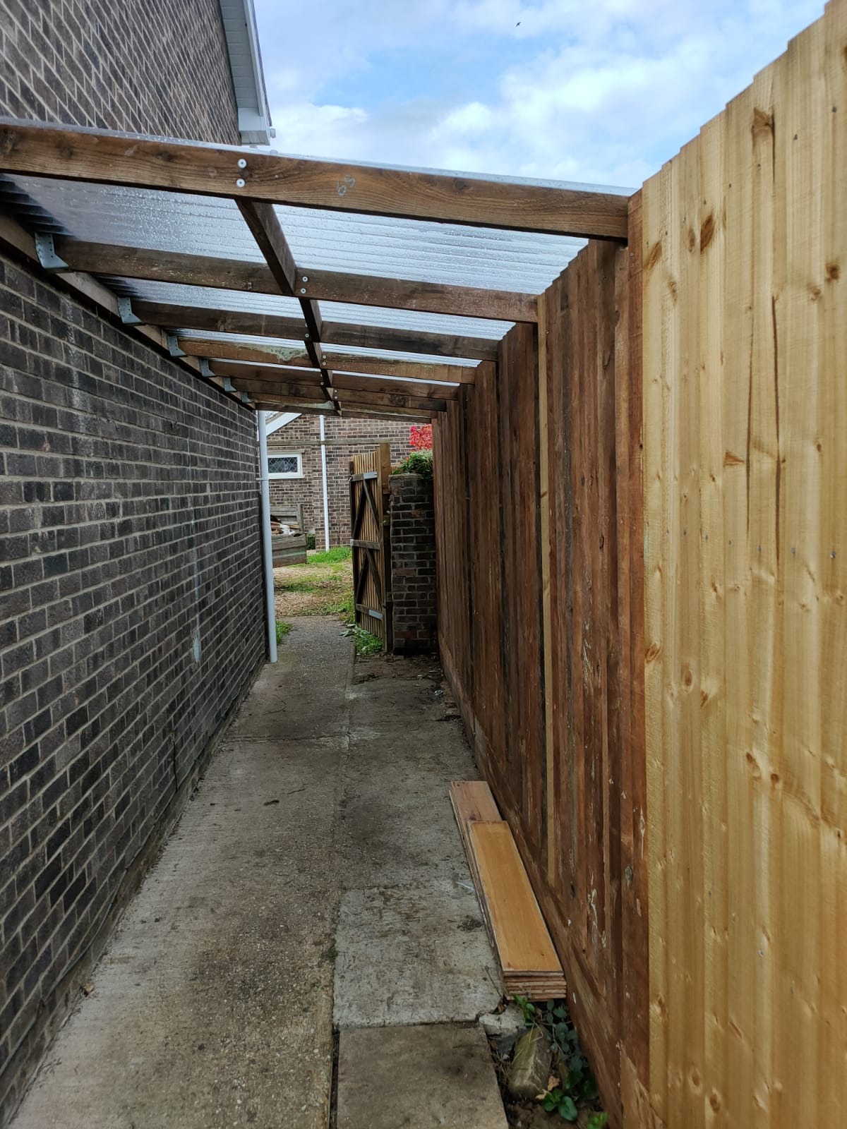 Lean-to showing struts joining fence to house wall with corrugated PVC roof