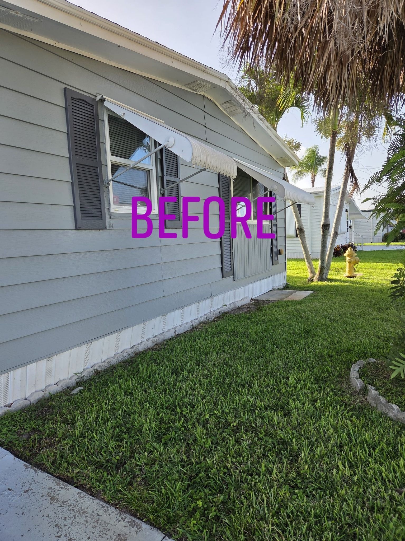 Exterior view of a light gray house with a partially retracted awning, green lawn, and sidewalk.