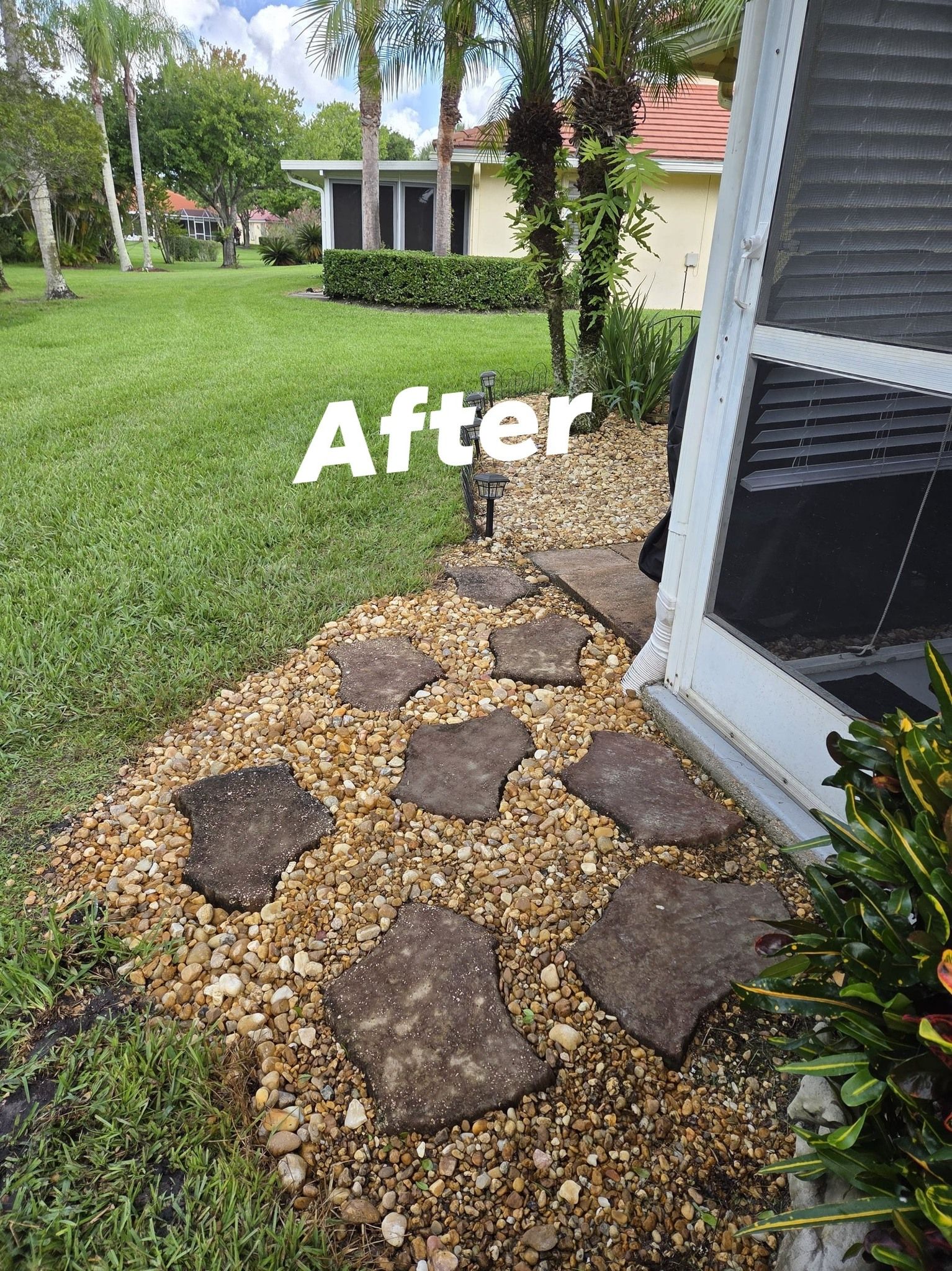 Stone walkway with gravel next to a house and green lawn.