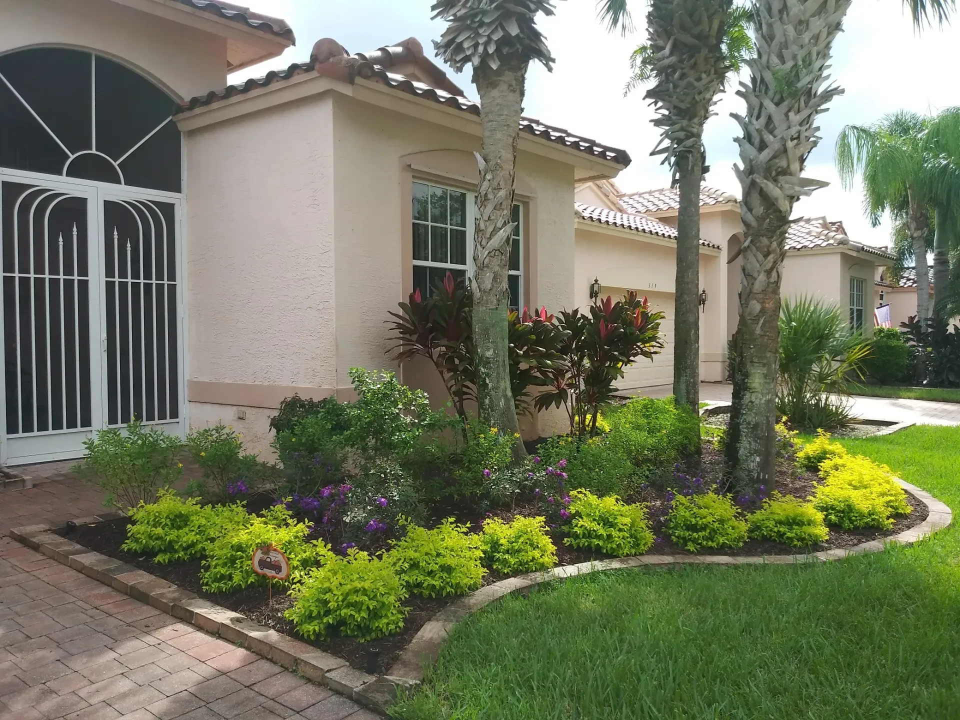 Beige stucco house with a manicured garden bed containing green and purple plants.