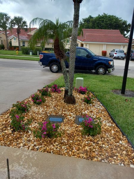 Landscaped island with pink flowers, tan rocks, and a blue truck parked in the background.