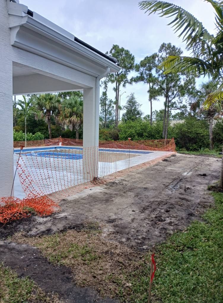 Pool under construction with unfinished brickwork and surrounding dirt path near a building with a covered patio.