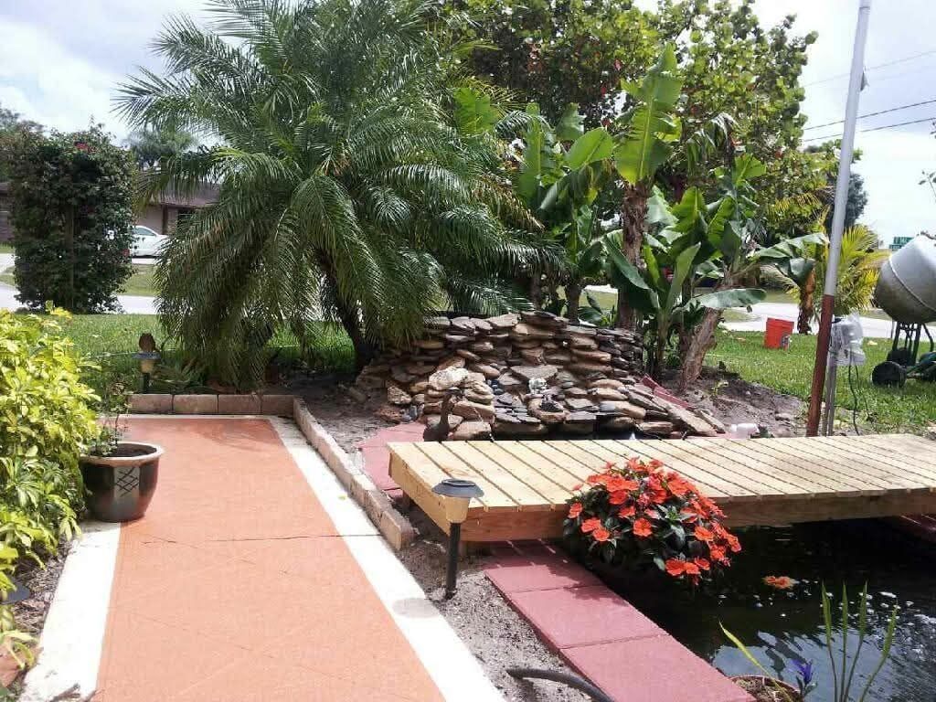 Backyard garden with pond, waterfall, wooden deck, palm tree, and banana plants.