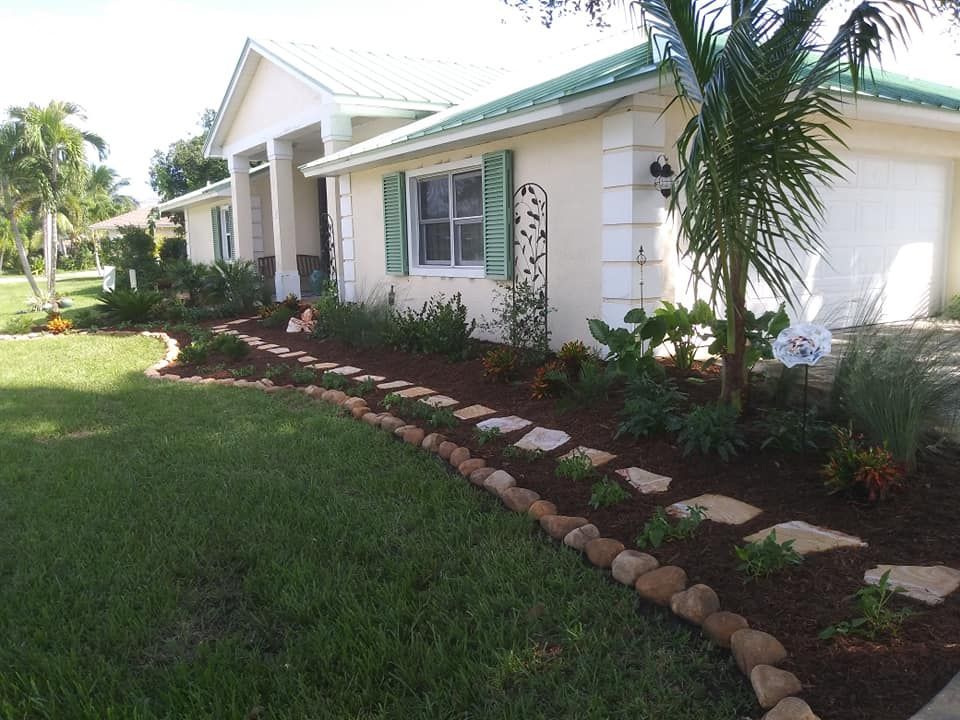 A one-story cream-colored house with green trim, a garden bed with stepping stones, and a green lawn.