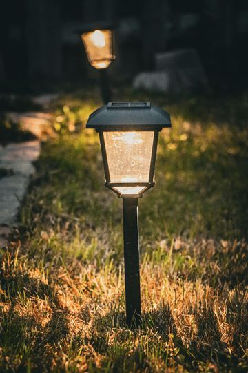 Two solar-powered garden lanterns glow softly in a grassy yard at dusk.