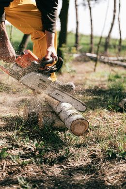 A person cutting a log with a chainsaw outdoors, sawdust flying.
