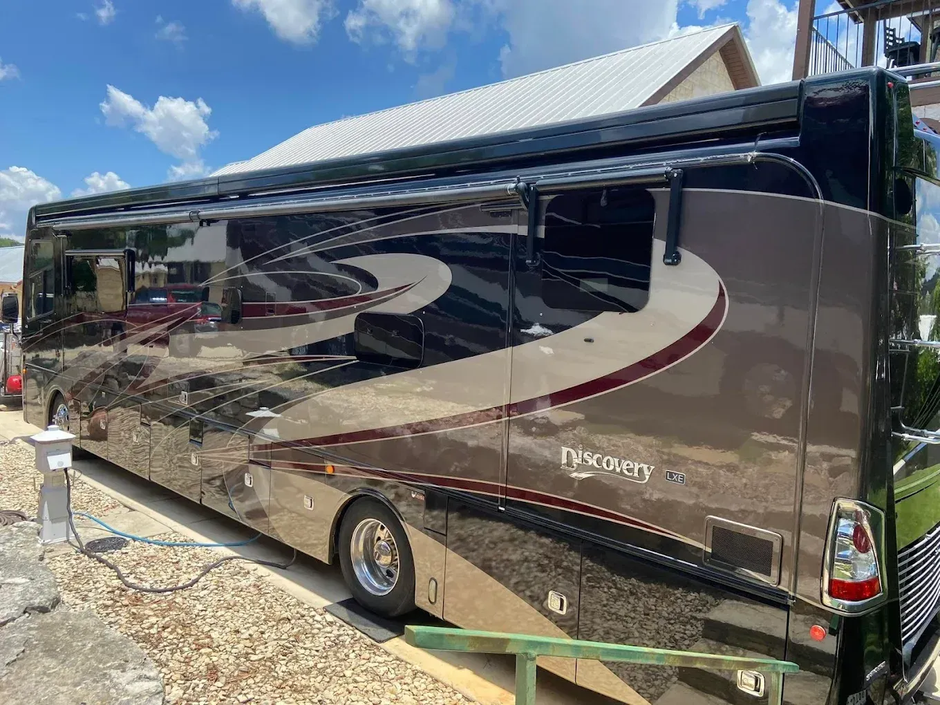Large black and silver motorhome parked on gravel under a blue sky.