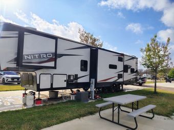 White Nitro travel trailer parked on grass beside a picnic table under a blue sky