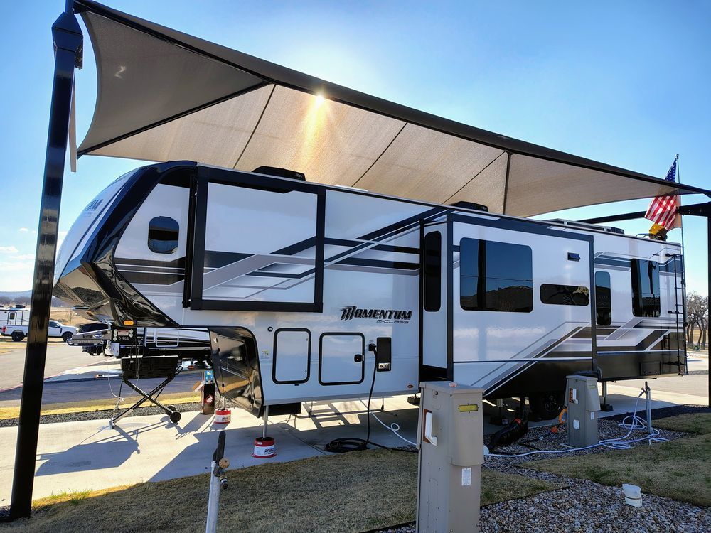 White and black travel trailer with extended awning parked outdoors in a sunny RV lot