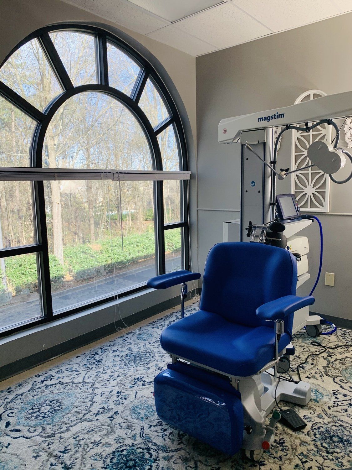 A blue chair is sitting in front of a large window in a room.