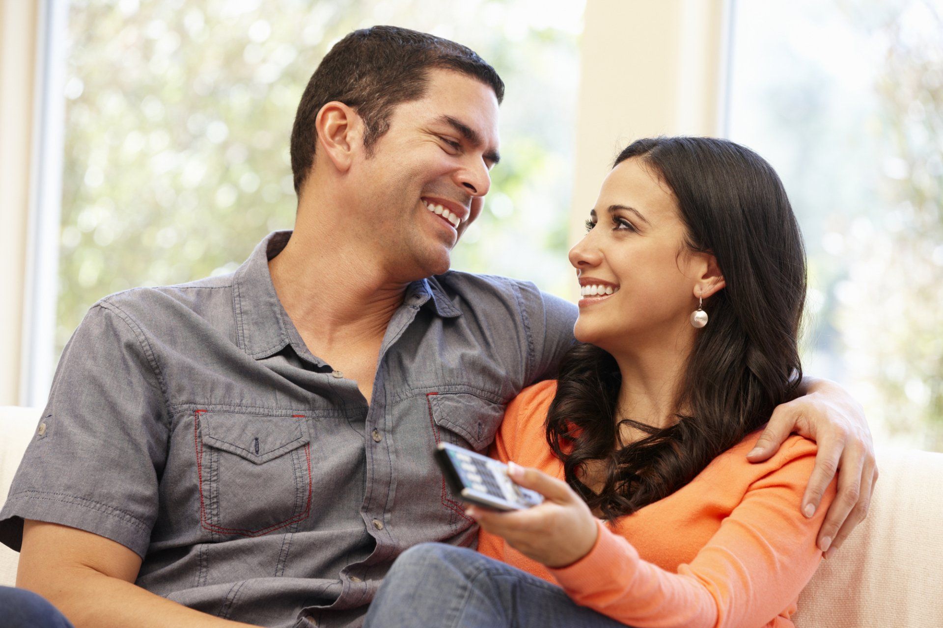 A man and woman are sitting on a couch looking at each other . the woman is holding a remote control.