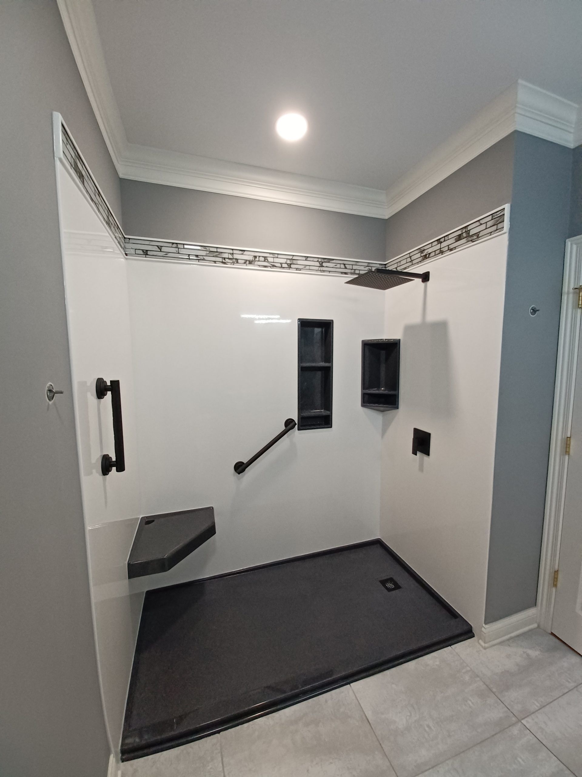 Accessible shower with black shower base, walls, and fixtures. White walls with gray accents, built-in seat and storage.