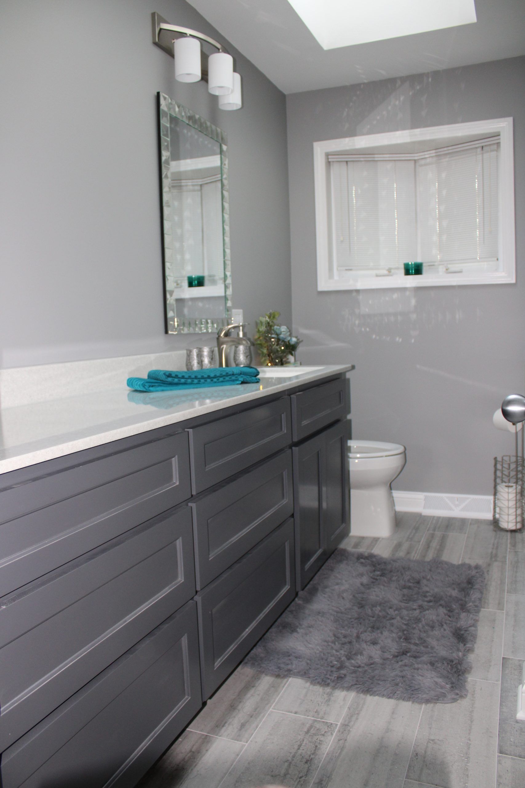 Gray bathroom with vanity, toilet, and fluffy rug. White countertop, cabinet doors, and trim.