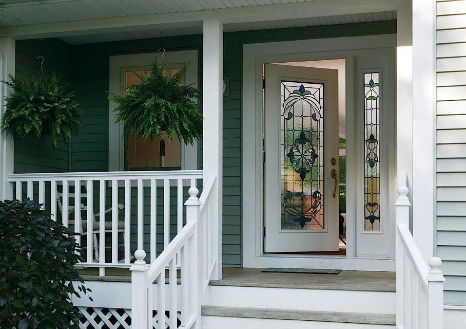 White porch with hanging ferns and decorative front door.