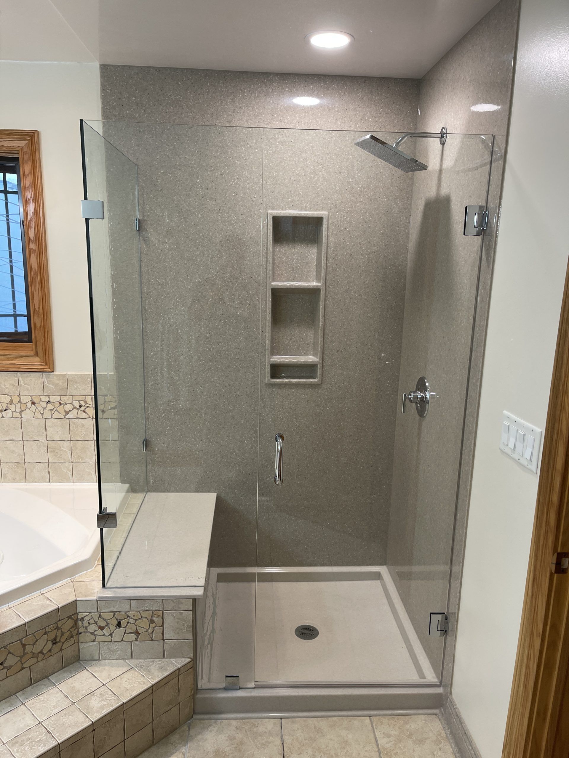 Modern shower with glass doors, built-in shelves, and a bench. Features neutral-colored tile and a rain showerhead.