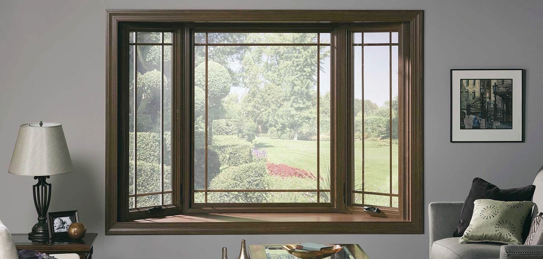 A brown-framed window with a view of a garden in a room with gray walls and a lamp.