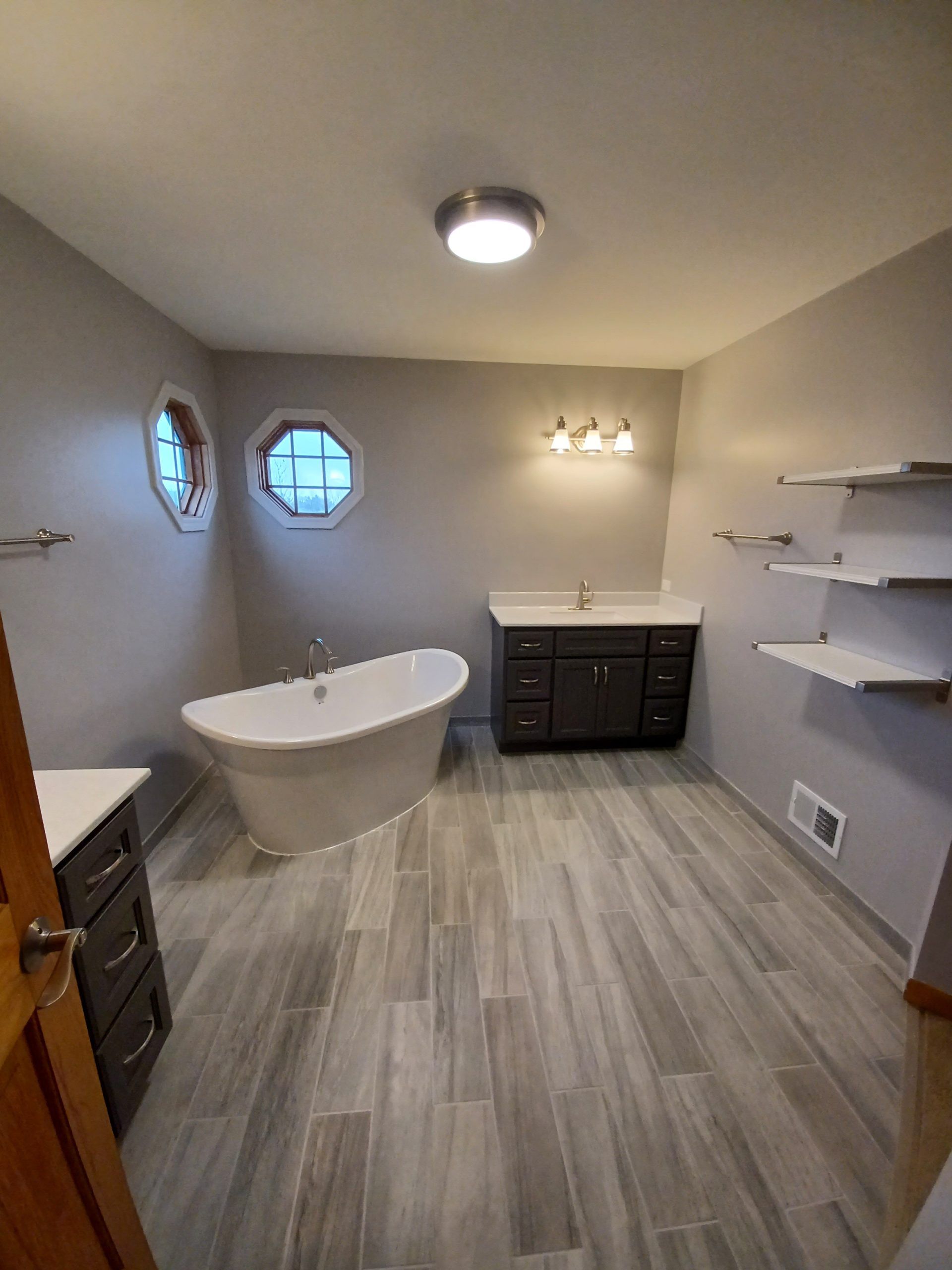 Modern bathroom with a freestanding tub, gray walls, and wood-look tile flooring.