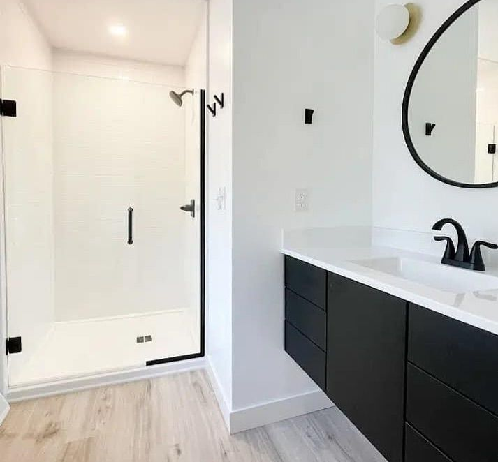 Modern bathroom with a glass shower, black vanity, and round mirror.
