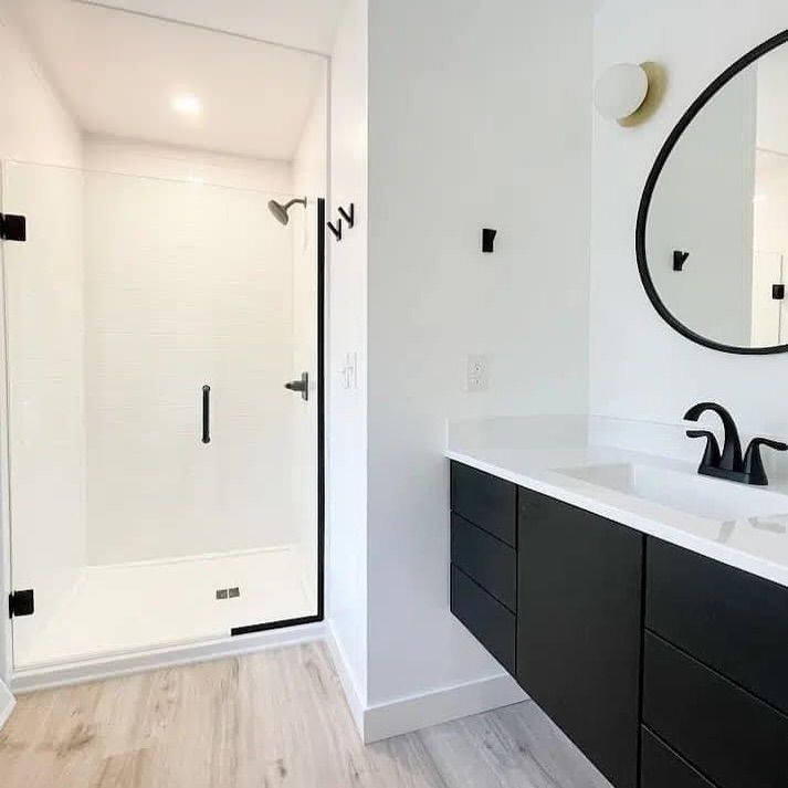 Modern white bathroom with black accents. Shower and floating vanity with black faucet and mirror.