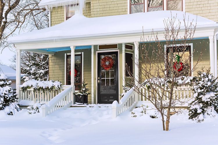 Snowy house porch with Christmas wreaths and greenery.