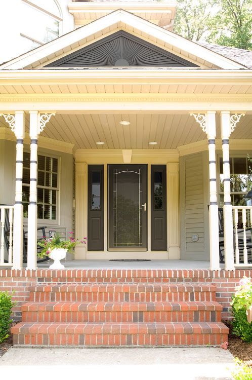 Brick steps lead to a house's covered front porch with a dark door, sidelights, and decorative columns.