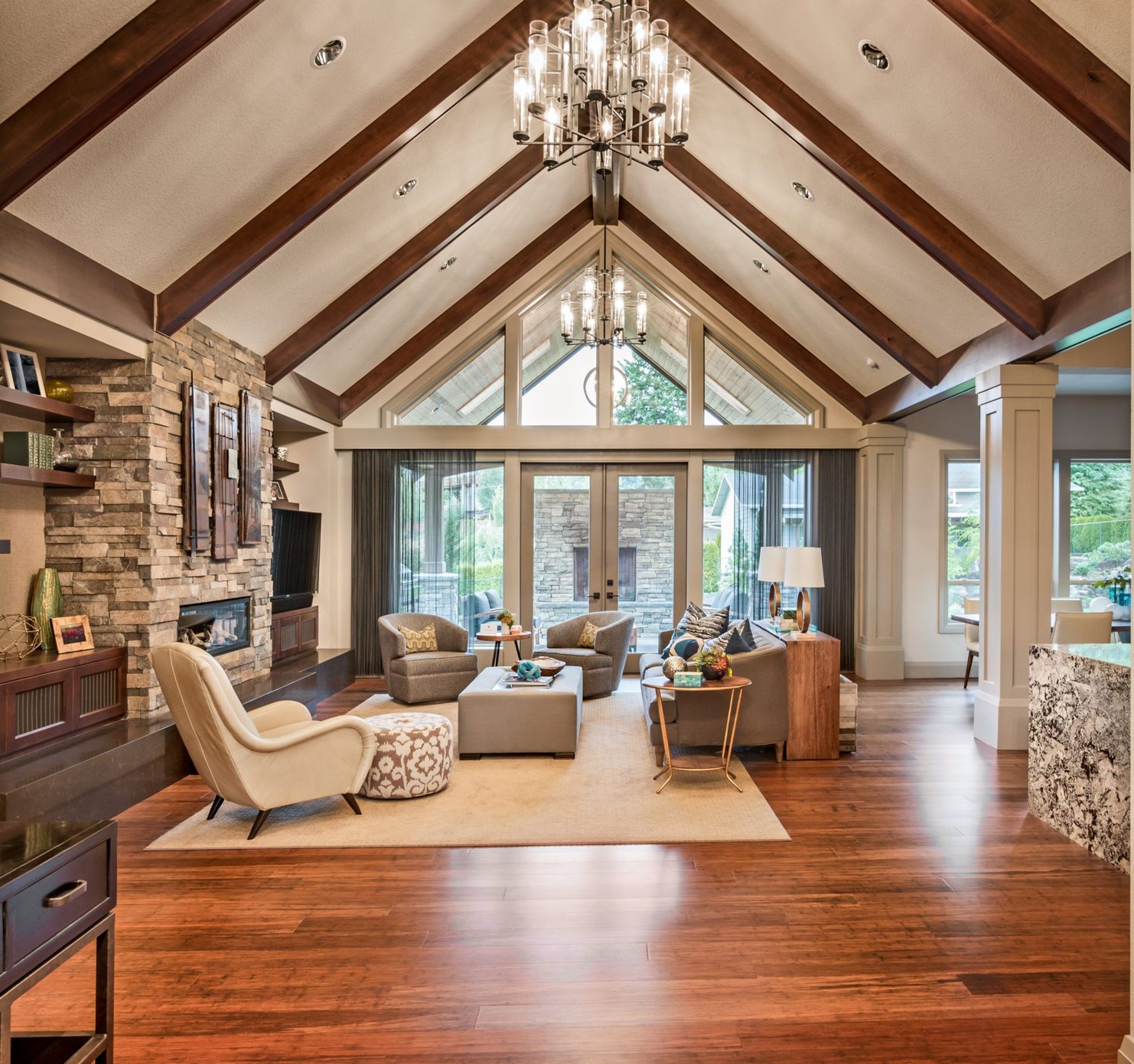 Living room with vaulted ceiling, stone fireplace, and large windows; wood floors and furniture.